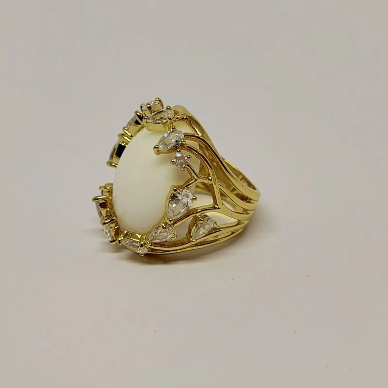 Anel dourado com cabochão branco oval em garras trabalhadas e cristais laterais — ref. ANQ0004A